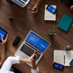 Overhead view of a diverse team discussing around a wooden table, using technology.